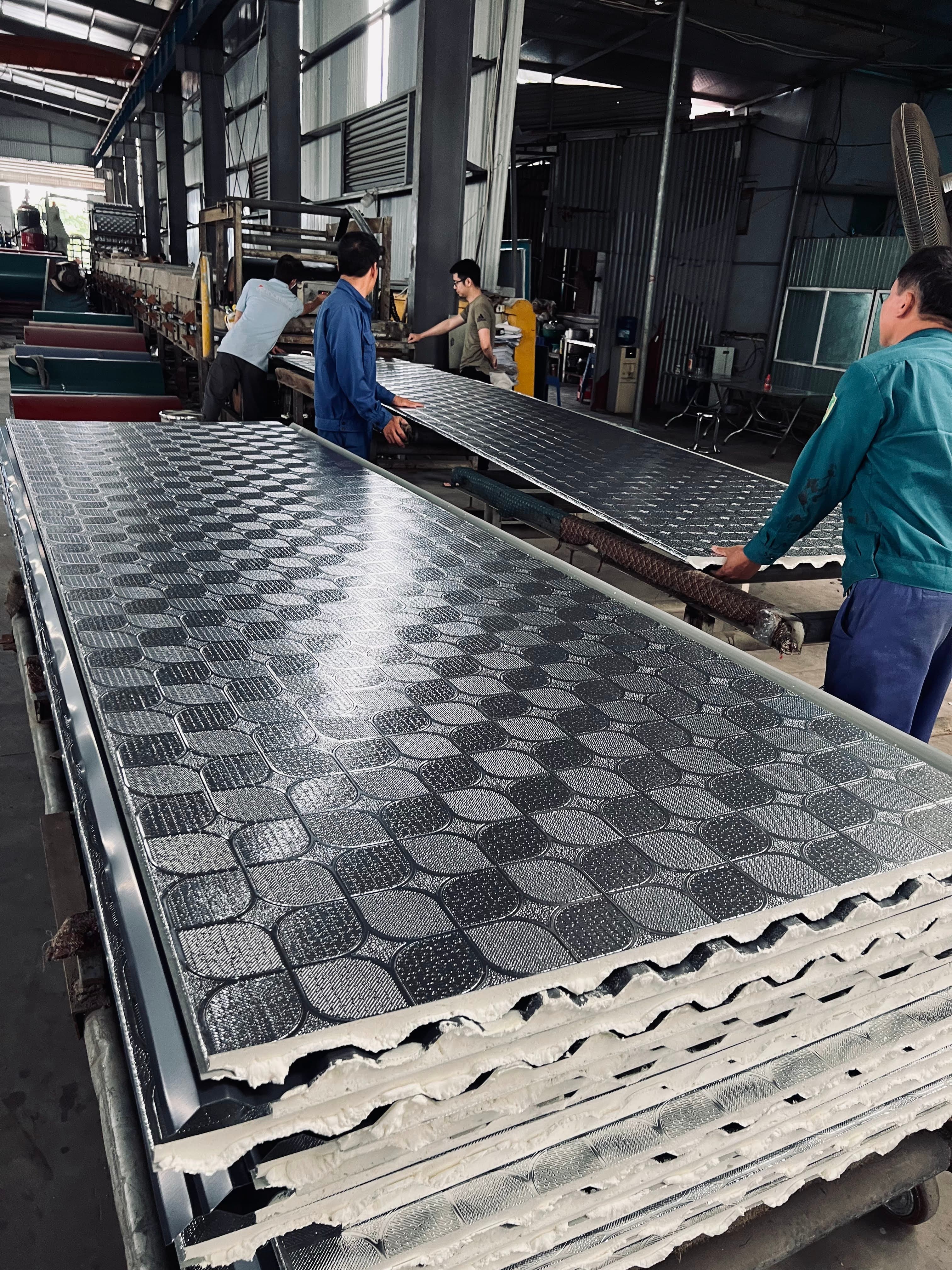 Workers handling embossed dark grey panels on a production line